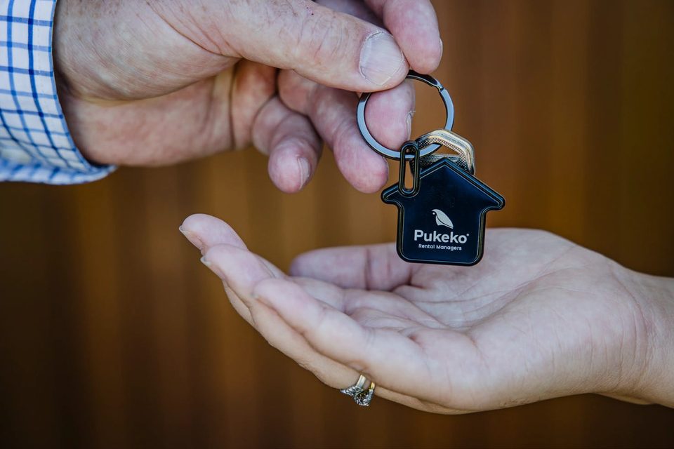 A Pukeko house-shaped keyring being handed into an open palm.