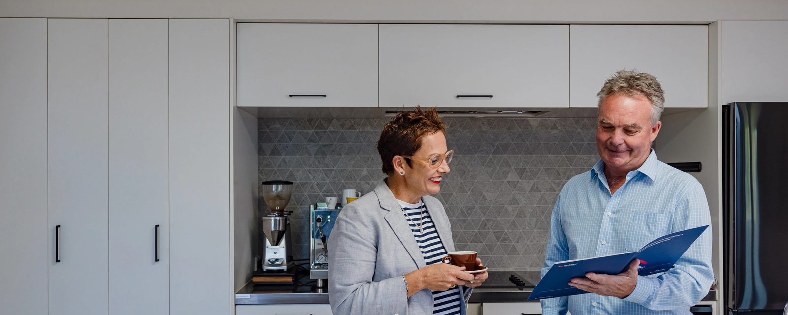 A rental manager and a property owner talking over a blue management folder in a kitchen.