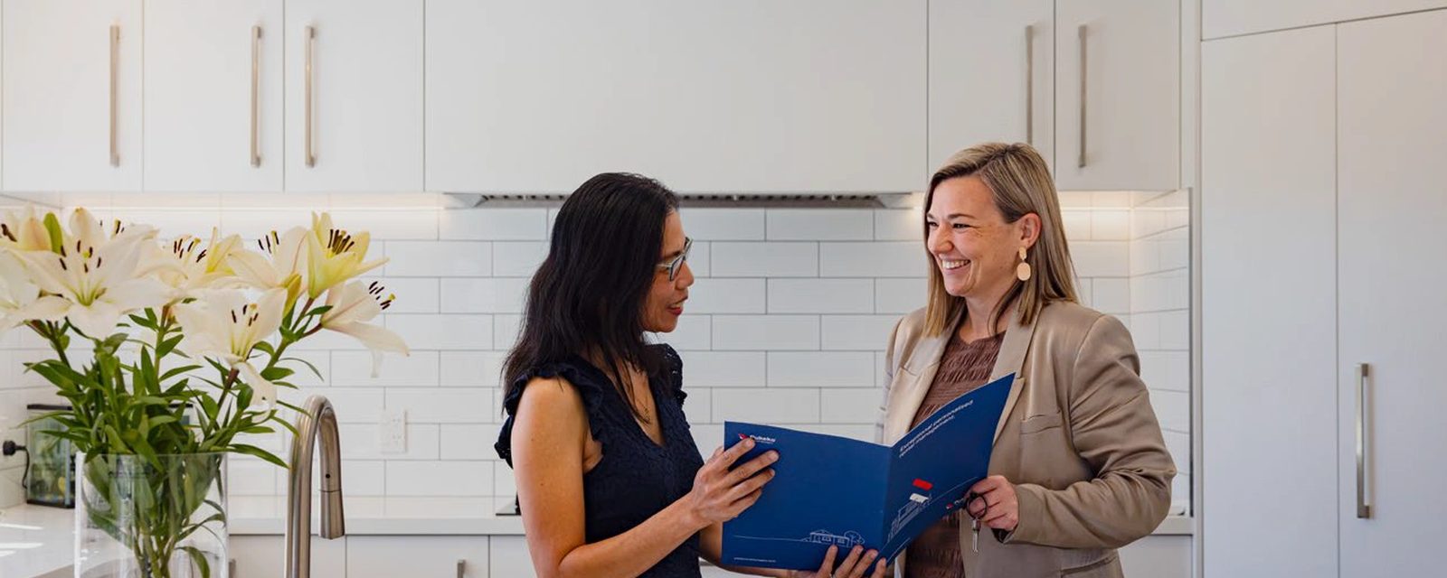 A rental manager going through a blue Pukeko management folder with a property owner in a kitchen.