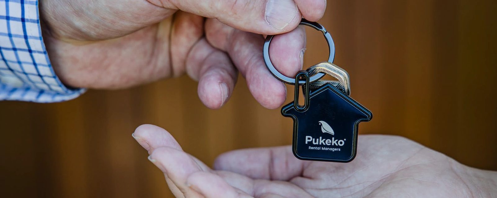 A hand holding out a Pukeko house-shaped keyring above an open palm.
